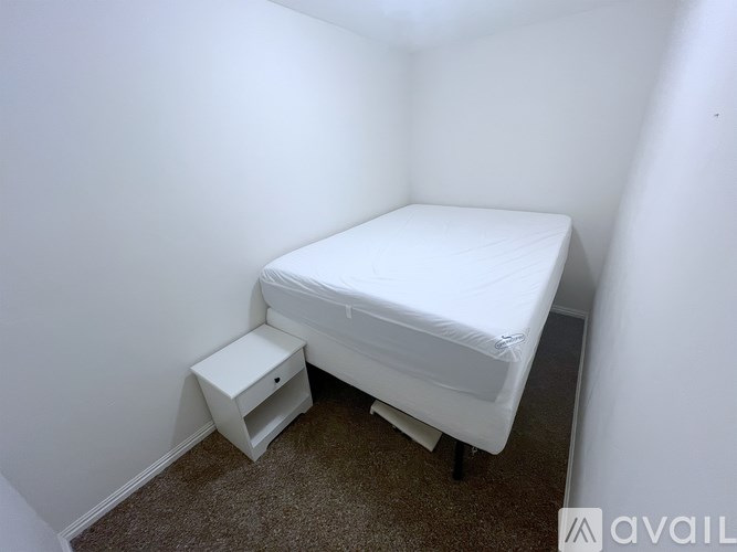 A white bed with a mattress and a small white nightstand.