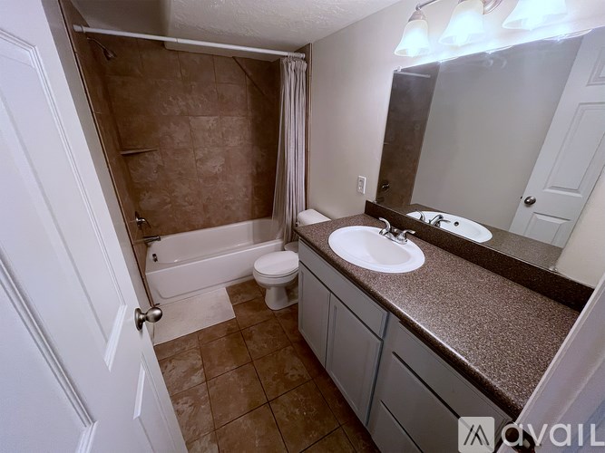 A bathroom with a brown tiled shower and a white toilet.