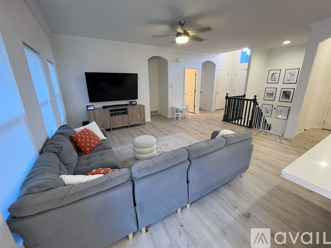 A living room with a grey couch, a television, and a ceiling fan.