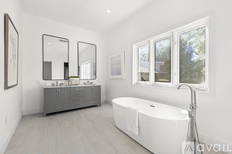 A bathroom with a white tub, a sink with a mirror above it, and a window with a view of trees.
