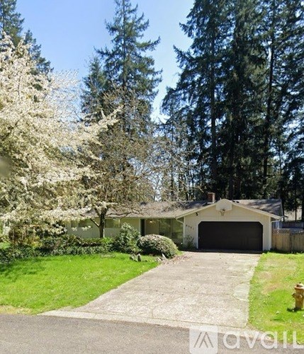 A house with a garage is surrounded by trees and has a white flowering tree in the front yard.
