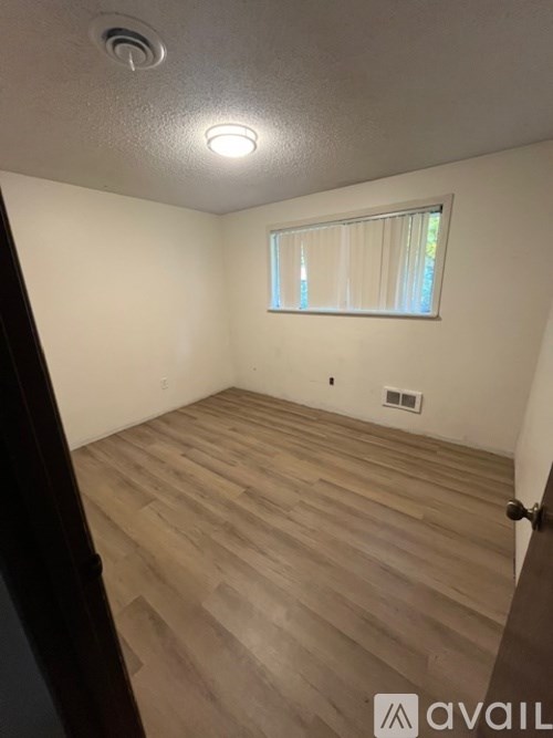 A room with wooden flooring and a window with blinds.