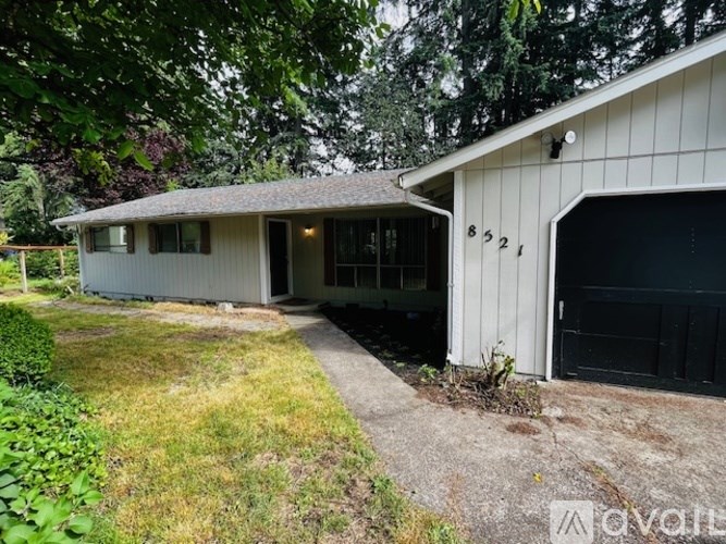A two-story house with a garage is surrounded by trees and grass.