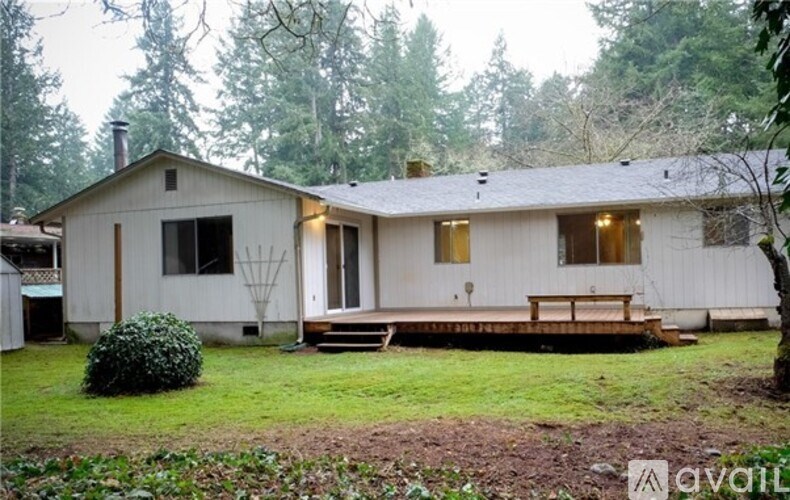 A house with a white exterior and a brown roof is surrounded by trees.