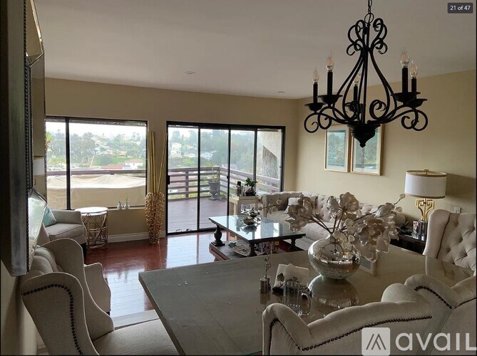 A living room with a chandelier, a couch, a coffee table, and a view of the outside.