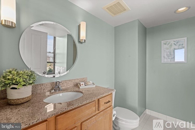 A bathroom with a round mirror, a sink, a toilet, and a plant.