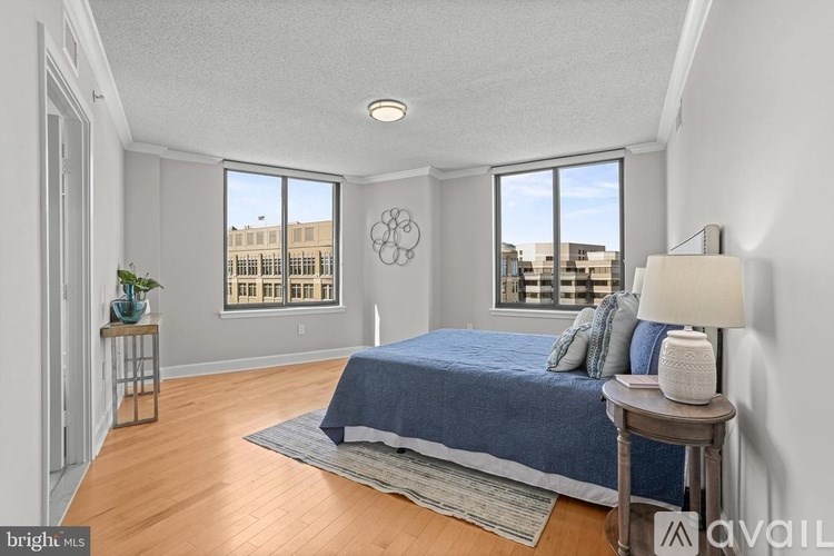 A bedroom with a bed, a side table, and a window overlooking a cityscape.