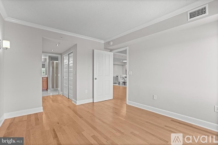 A spacious room with wooden floors and white walls, with a door open to another room.