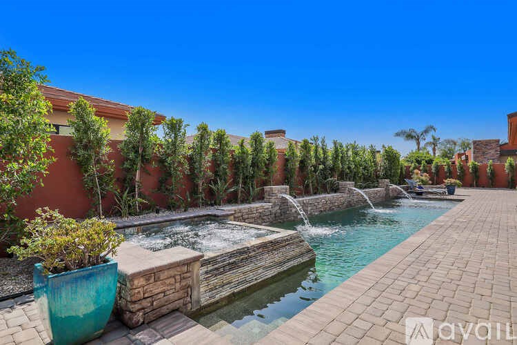 A pool with a waterfall surrounded by a brick wall and green plants.