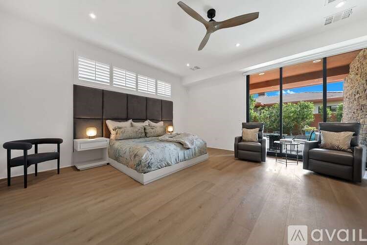 A bedroom with a bed, two chairs, and a table with a fan on the ceiling.