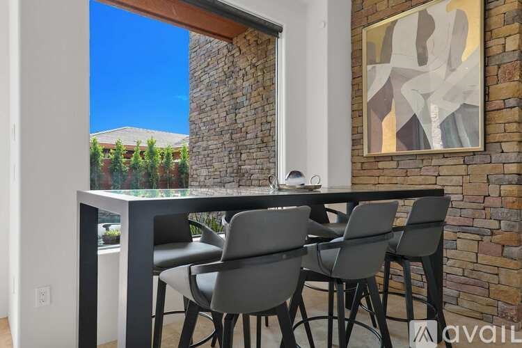 A dining table with four chairs is set against a brick wall with a painting hanging above it.