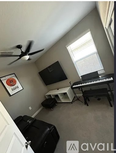 A room with a ceiling fan, a piano, and a bag on the floor.
