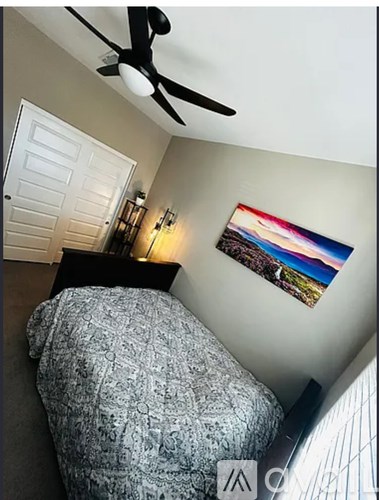 A bedroom with a bed, a ceiling fan, and a painting on the wall.
