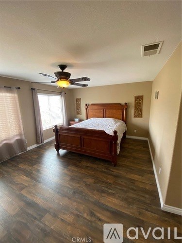 A bedroom with a bed, wooden floors, and a ceiling fan.