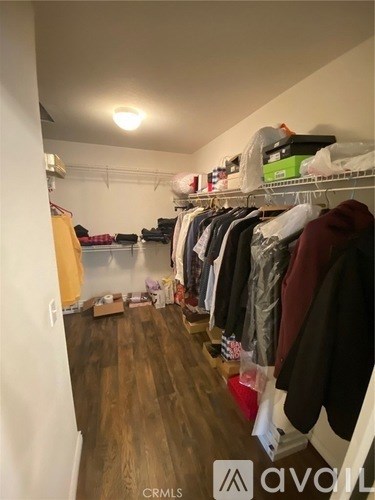 A room with a wooden floor and a white wall with a closet full of clothes.
