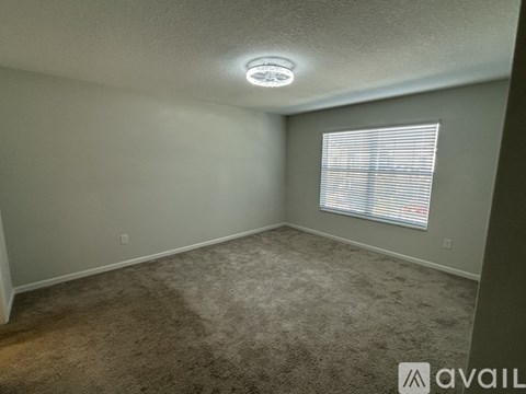 A room with a carpeted floor, a window with blinds, and a smoke detector on the ceiling.