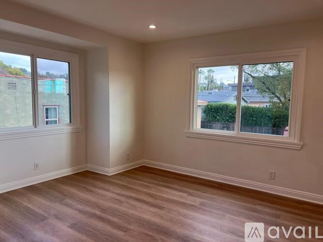 A room with wooden flooring and two windows.
