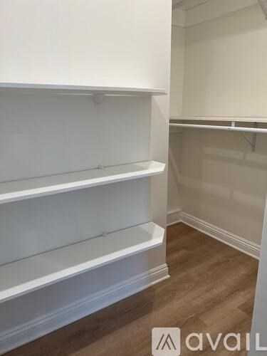 A white shelving unit with three shelves is in a room with wooden flooring.