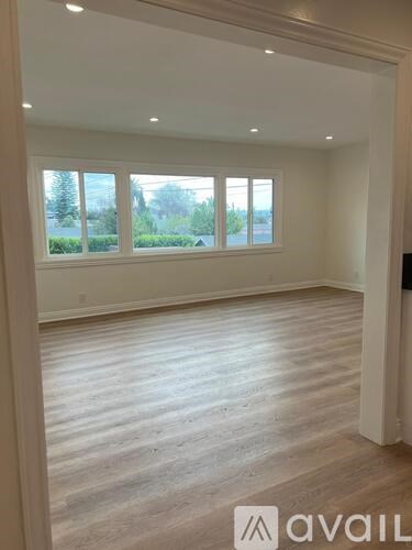 A room with wooden flooring and a large window overlooking a garden.
