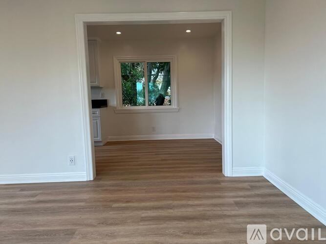A room with wooden flooring and a window overlooking a tree.