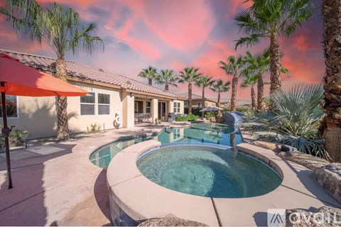 A pool surrounded by palm trees and a house.
