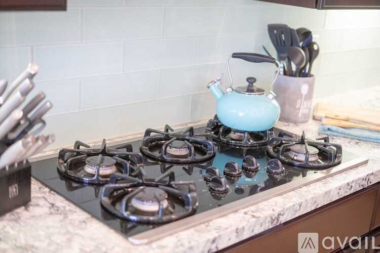 A teapot is on a stove with four burners lit.