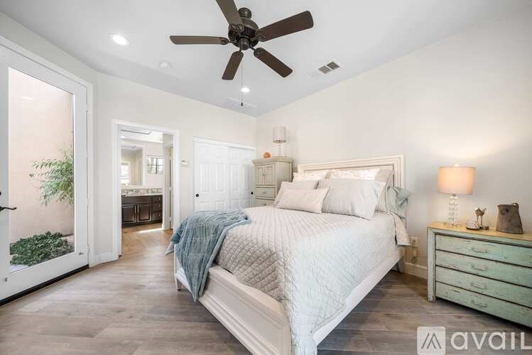 A bedroom with a large bed, a ceiling fan, and a dresser with a lamp on it.