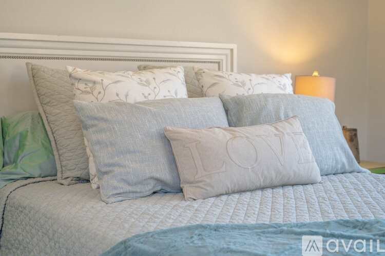 A bed with a white headboard and a blue comforter with four pillows on it.