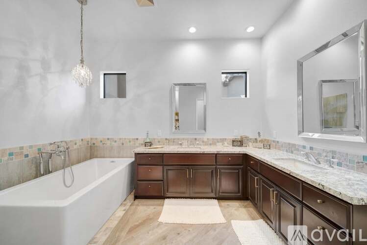 A bathroom with a white tub, wooden vanity, and a chandelier.