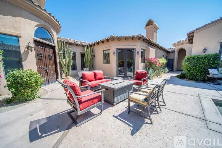 A patio with red chairs and a table is in front of a house.