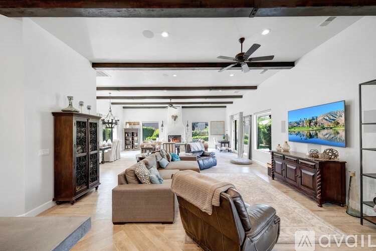 A spacious living room with a brown leather sofa and a large TV mounted on the wall.