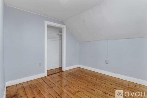 A room with wooden floors and white walls, with a doorway leading to another room.