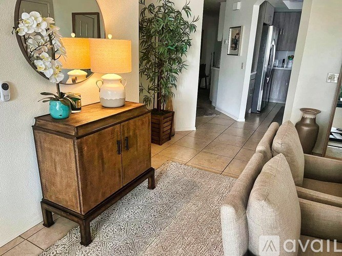 A wooden cabinet with a vase of flowers on top sits in a room with a rug and a mirror.