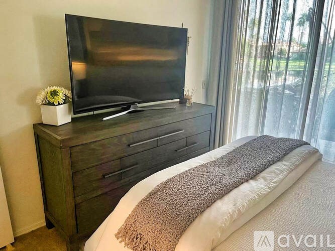 A bedroom with a bed, a dresser with a television on top, and a window with curtains.