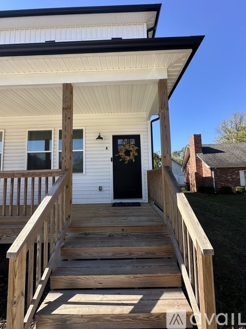 A white house with a black door and a wooden deck.