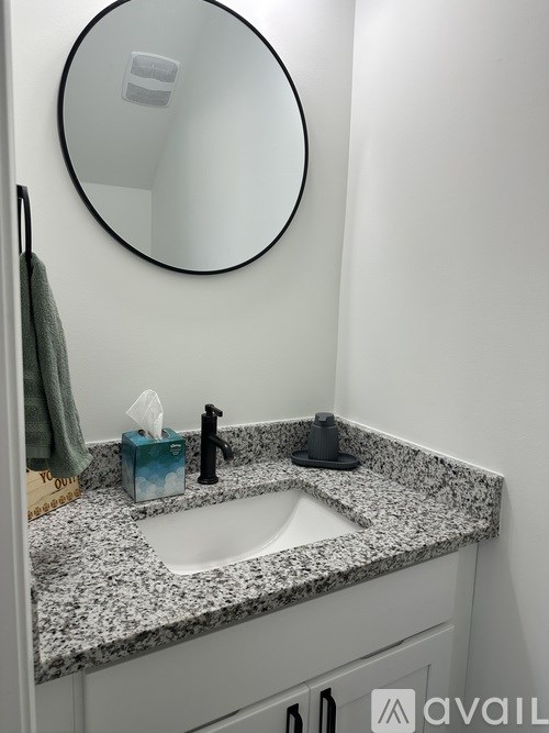 A bathroom with a granite counter top and a round mirror.