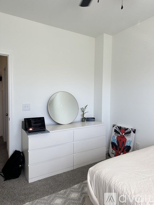 A white bedroom with a round mirror and a pillow with a spider on it.