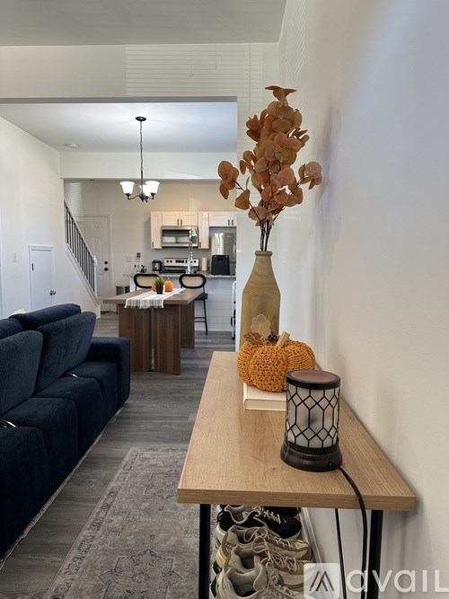 A living room with a dark blue couch and a wooden table with a vase and pumpkin on it.