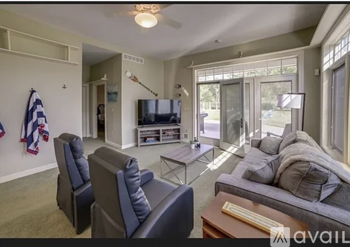 A living room with a grey couch, a black chair, a glass coffee table, a flat screen TV, and a ceiling fan.