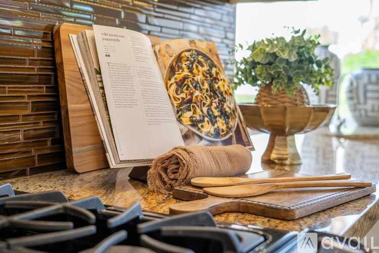 A kitchen counter with a book, a plant, and a wooden cutting board.