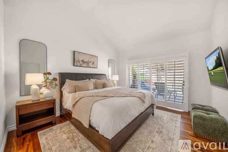A bedroom with a large bed, a nightstand with a lamp, a chair, and a painting on the wall.