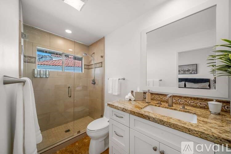 A bathroom with a marble countertop and a glass shower stall.
