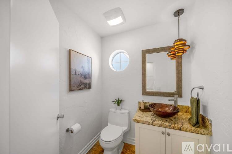 A bathroom with a toilet, sink, mirror, and a plant.
