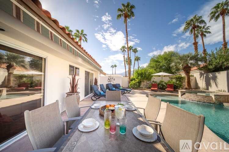 A table set for a meal outside a house with a pool and palm trees.