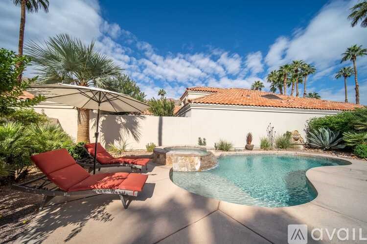A pool surrounded by red lounge chairs and palm trees.