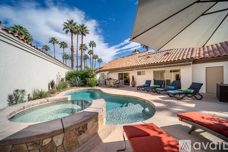 A pool with a hot tub and lounge chairs in front of a house with palm trees.