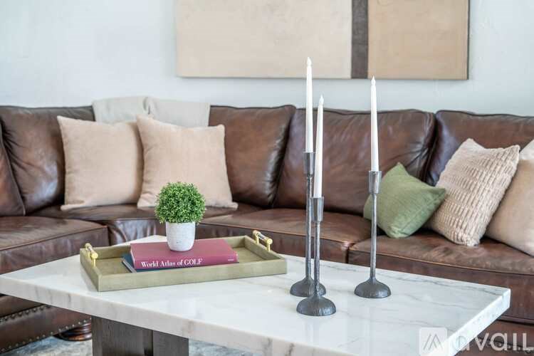 A living room with a brown leather couch, a marble coffee table, and a tray with a book and a plant on it.