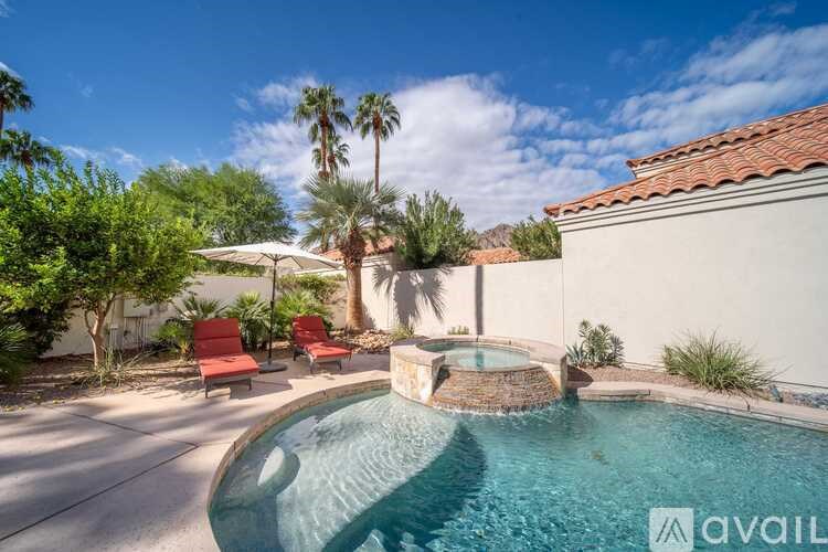 A pool with a waterfall and two red chairs.