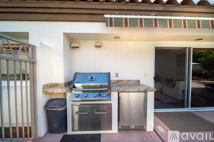 A house with a grill and a trash can outside.