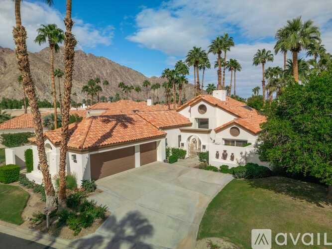 A house with a red tile roof is surrounded by palm trees.